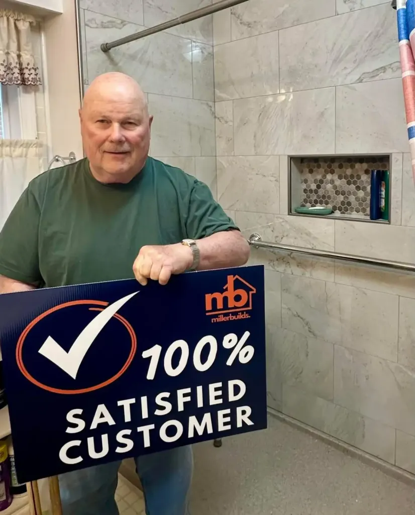 Miller Builds customer holding a 100% Satisfied Customer sign in his newly remodeled walk-in shower